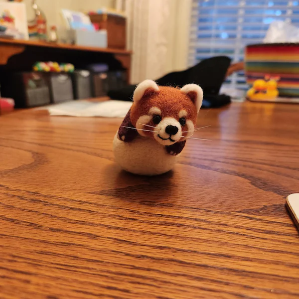A needle-felted red panda on a wooden table